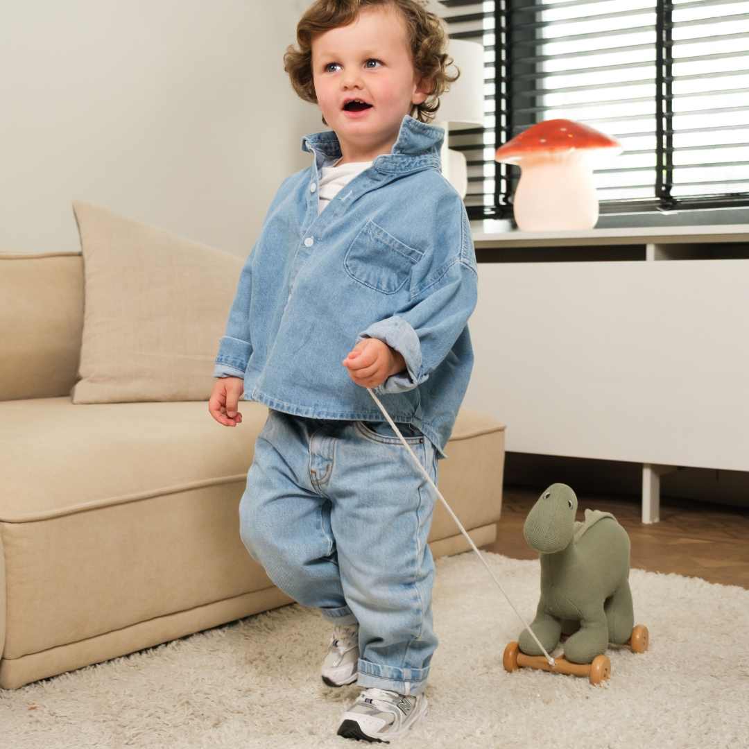 Een peuter trekt de groene dinosaurus Victor trekfiguur over een vloerkleed.