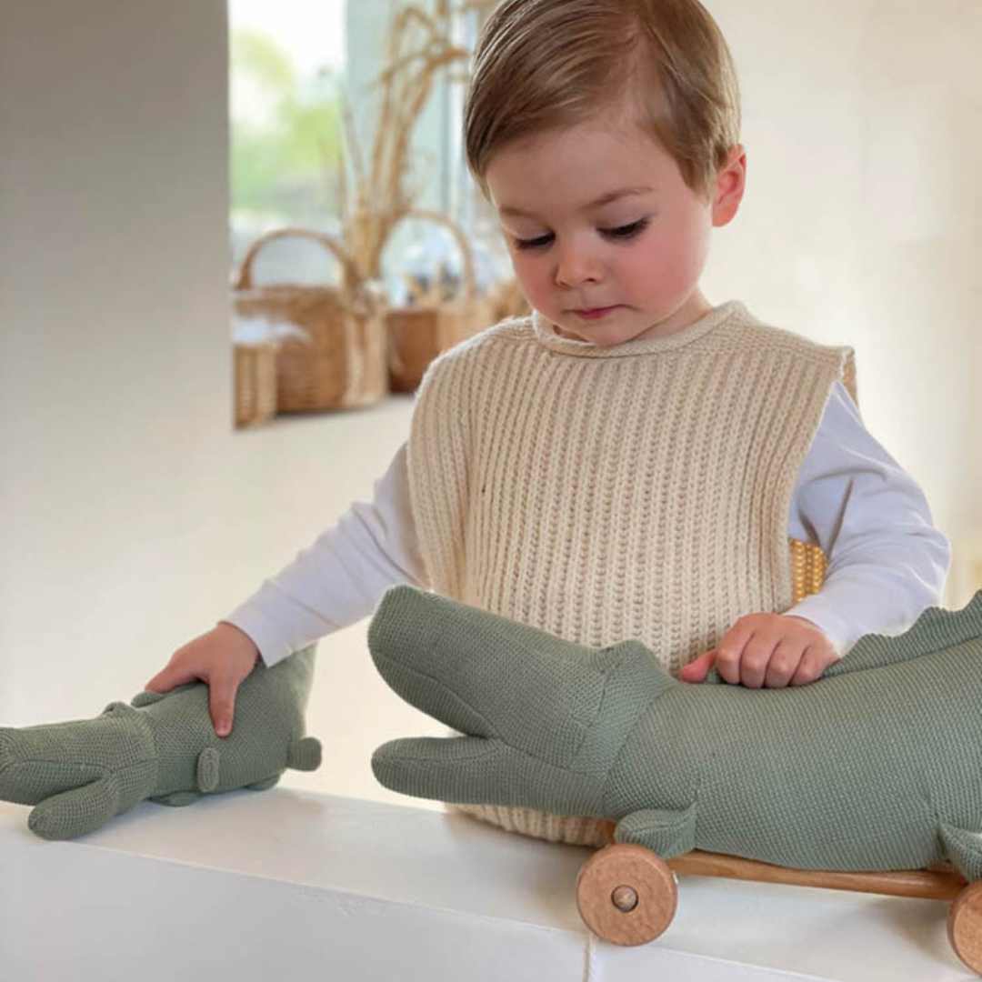 Een kind speelt met een grote Egmont Toys krokodil trekfiguur en een kleinere knuffelkrokodil.