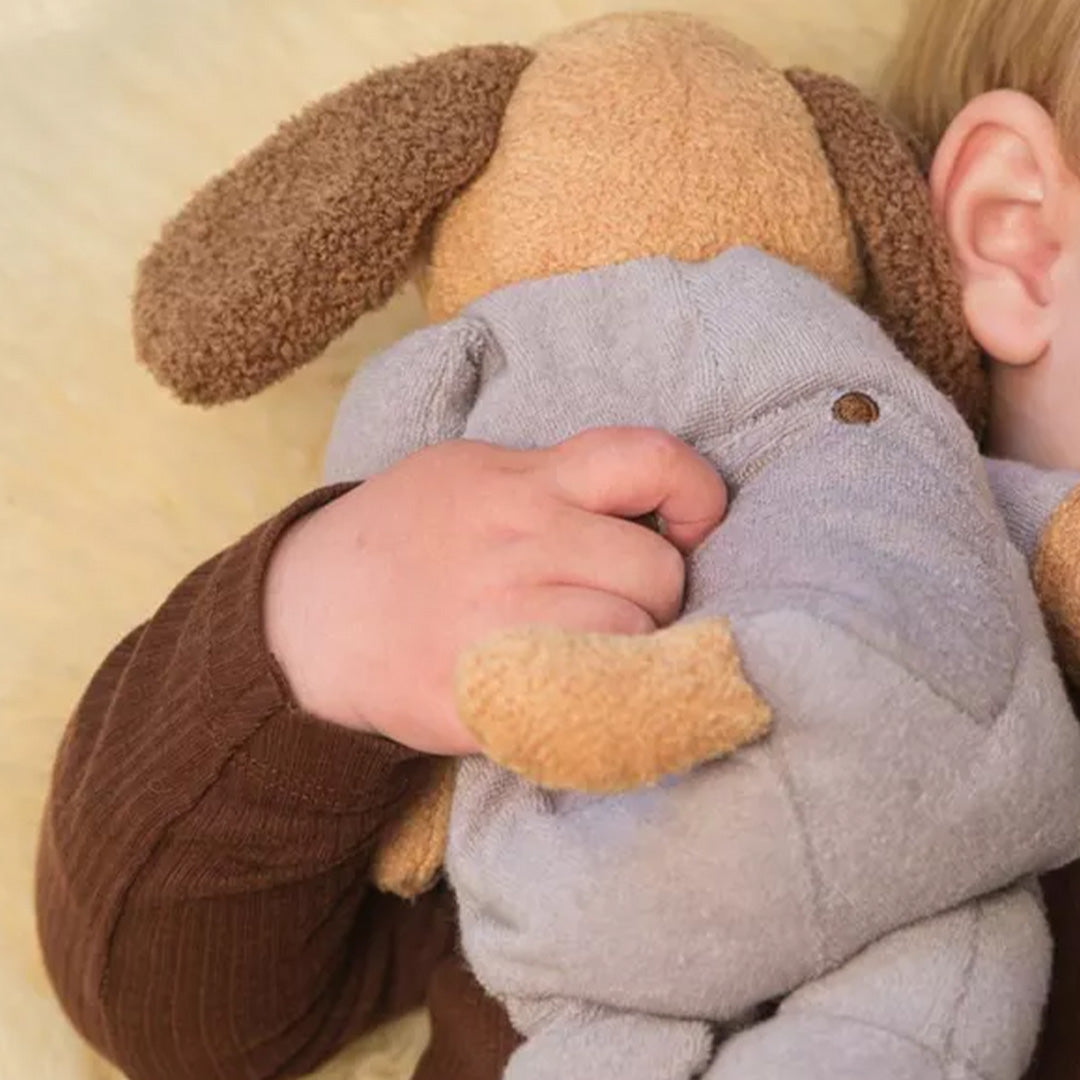 Een kinderhand houdt de achterkant van de Egmont Toys pluchen verzwaarde hond vast.