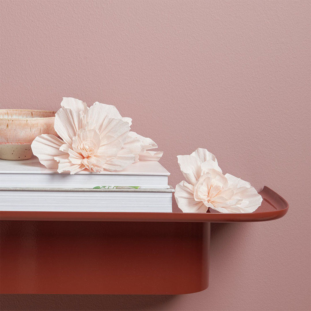 Twee roze crêpepapier bloemen als decoratie op een stapel boeken op een plank.