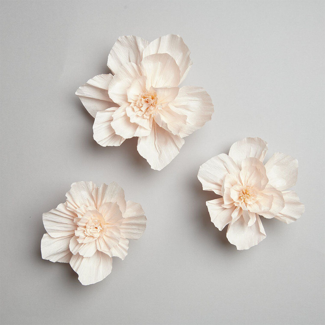 Drie roze crêpepapier bloemen los op een lichtgrijze achtergrond.