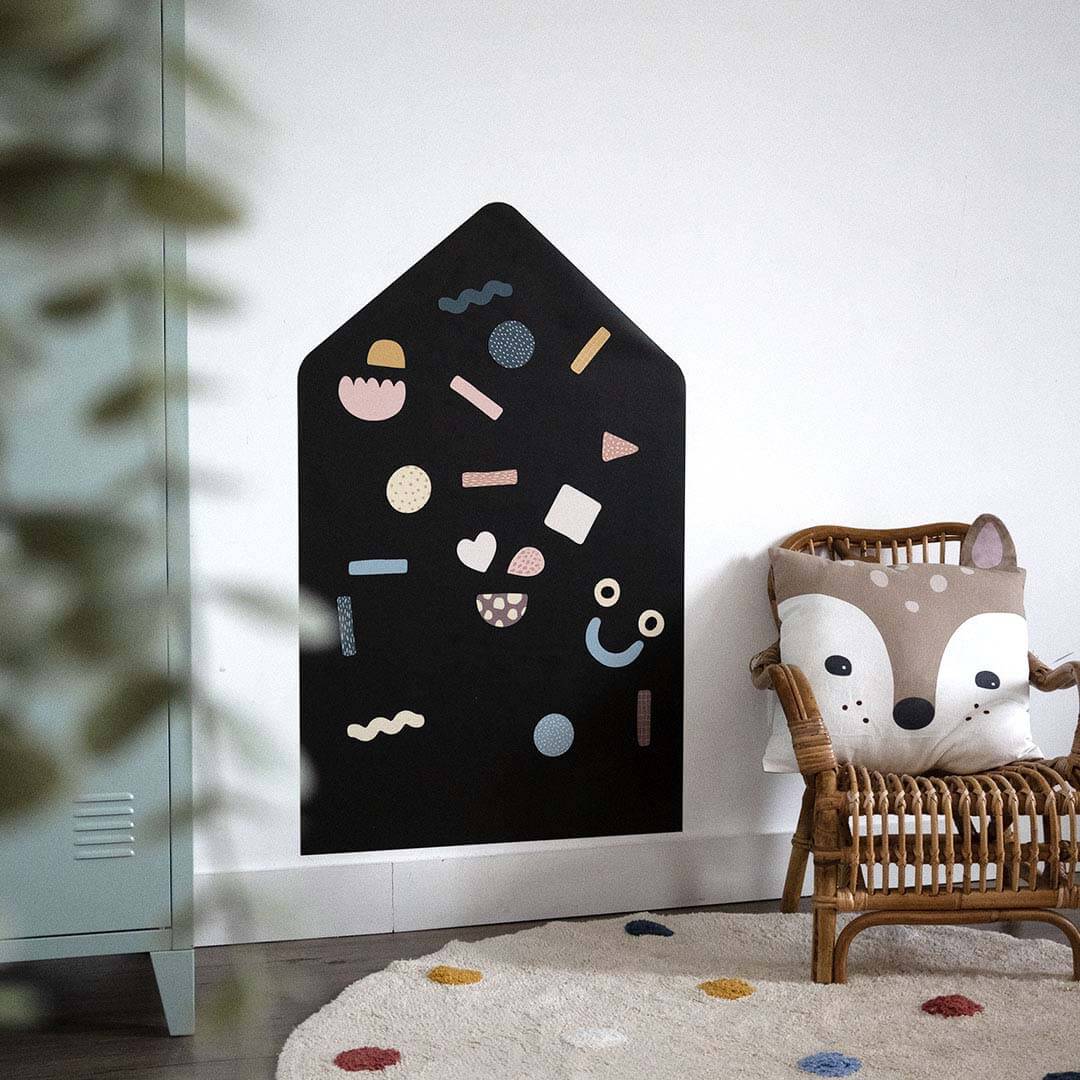 Zwart Ferflex magneetbord in huisvorm met kleurrijke geometrische magneten aan een witte muur.