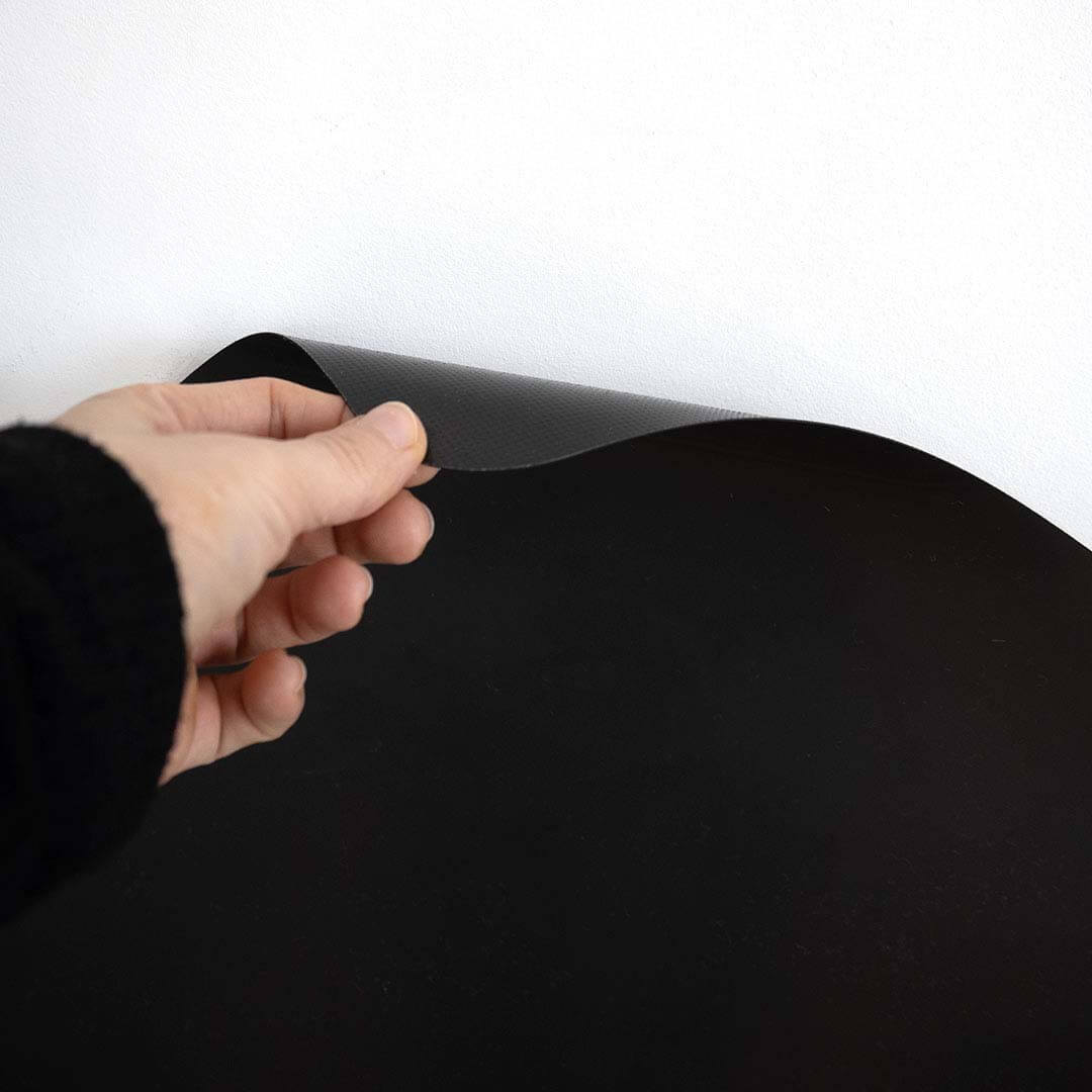 Een hand trekt een hoek van het flexibele Ferflex magneetbord los van de muur.
