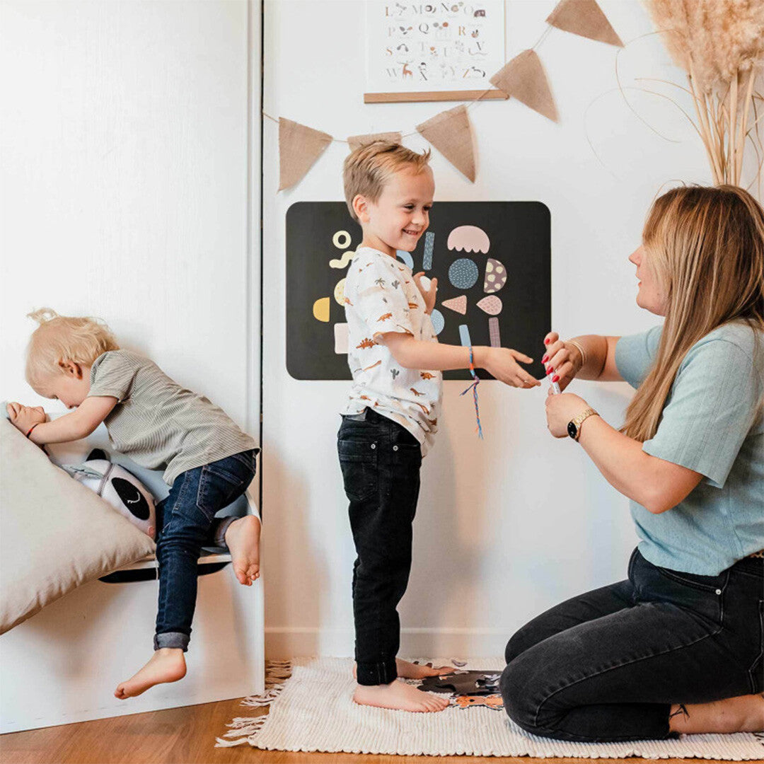 Een kind en volwassene spelen met het ferflex zwarte magneetbord met kleurrijke magnetische vormen.
