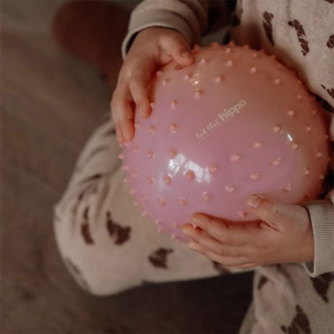 Kinderhanden houden een roze find that hippo sensorische bal met textuur vast.