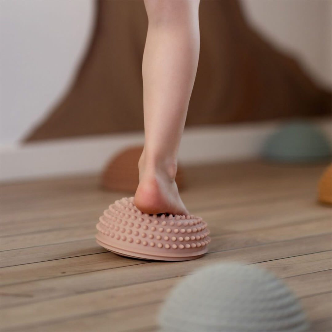 Een kind stapt met blote voet op een roze find that hippo sensorische stapsteen op een houten vloer.