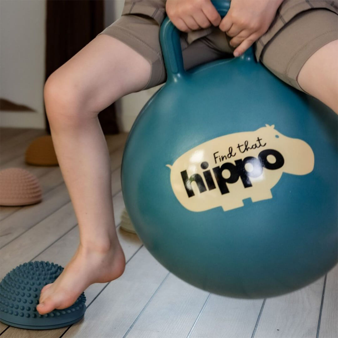 Detail van een kind dat op de find that hippo skippybal zit, met een voet op een textuurbal.