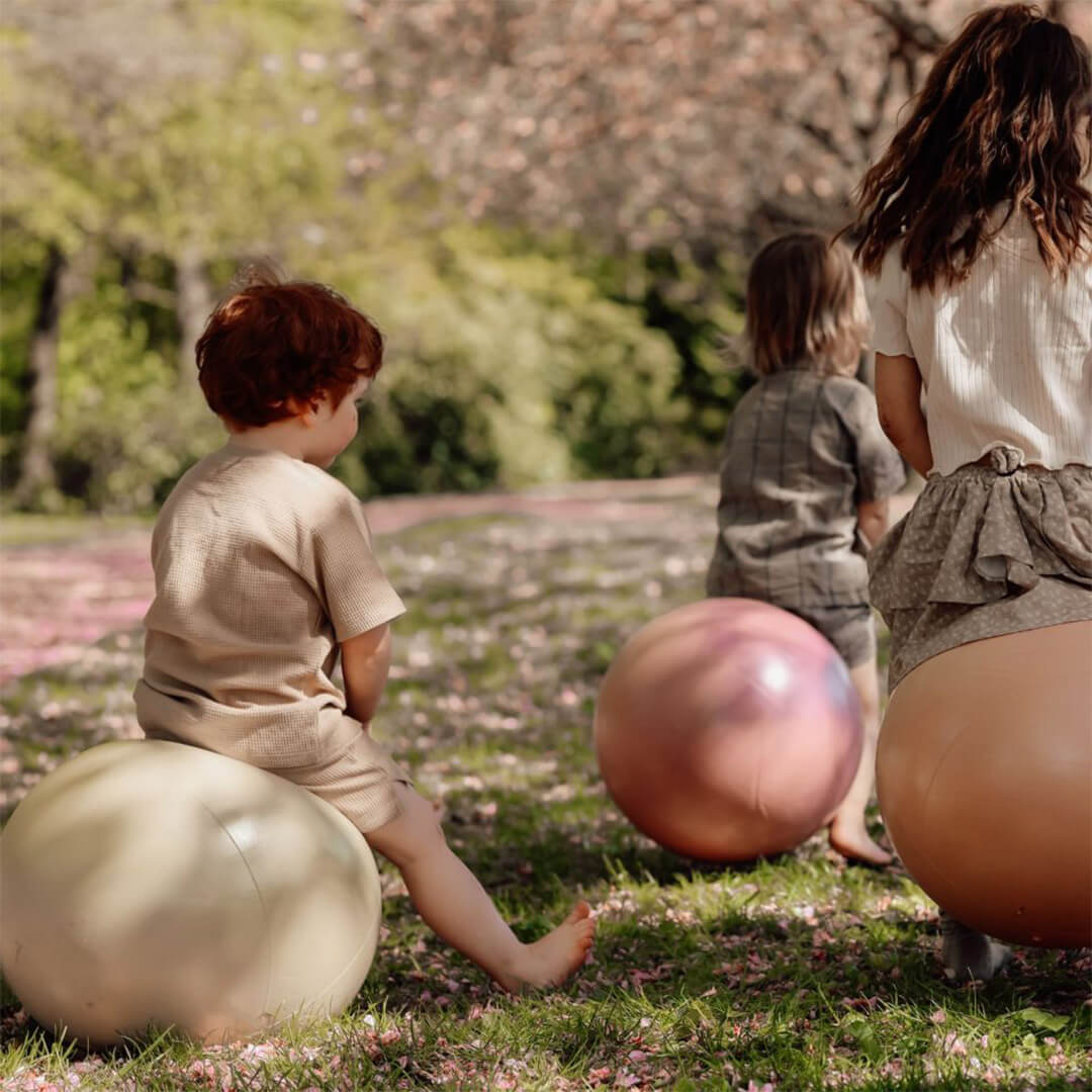 Drie kinderen zitten op Find that hippo skippyballen in een park vol roze bloesem.
