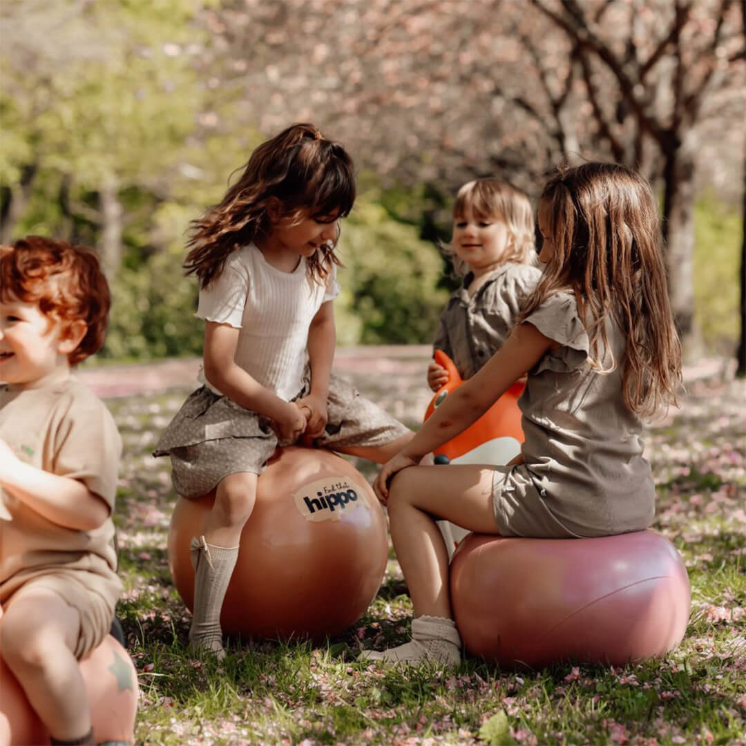 Drie kinderen spelen met find that hippo skippyballen in een park met bloesem.