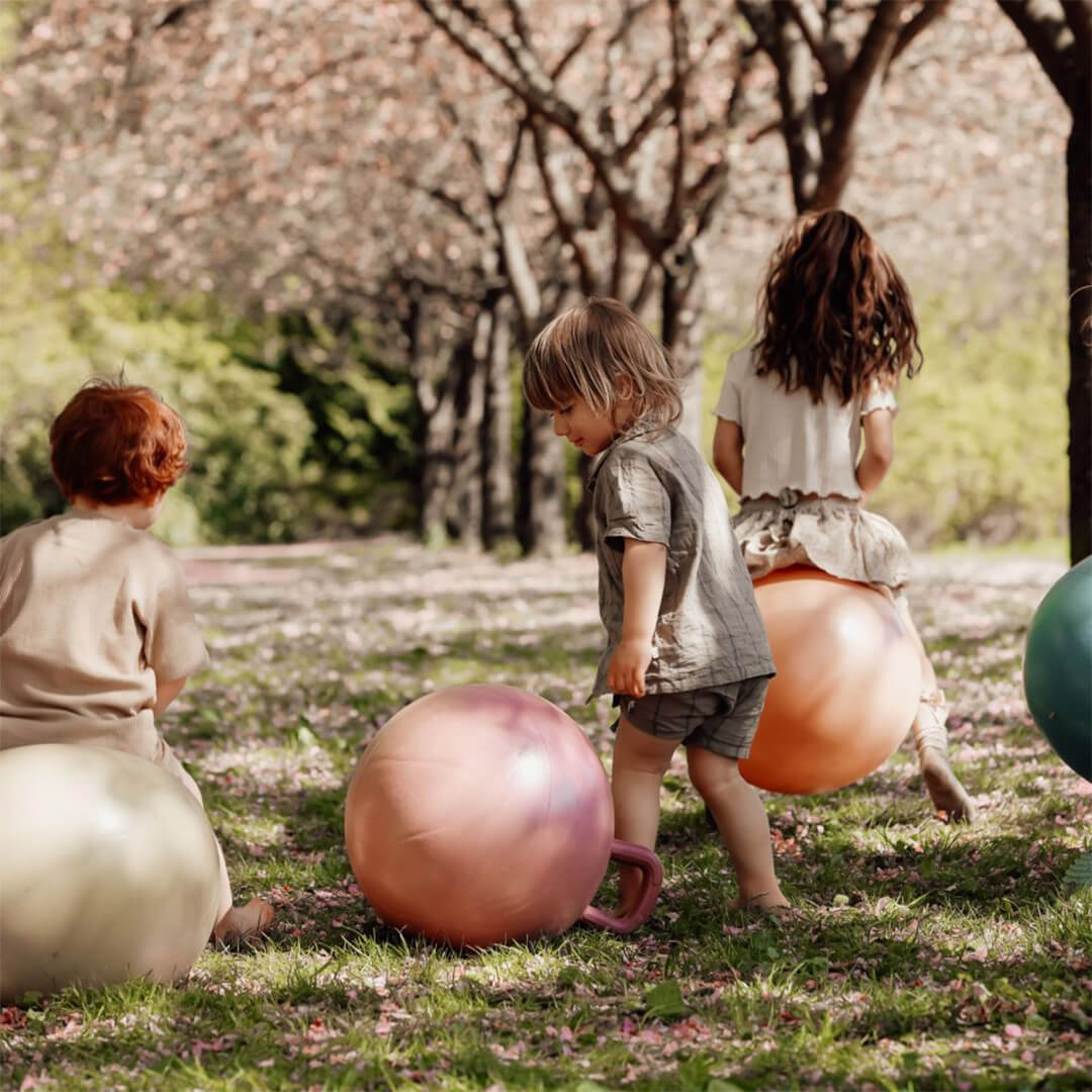 Drie kinderen spelen met find that hippo skippyballen in een park.