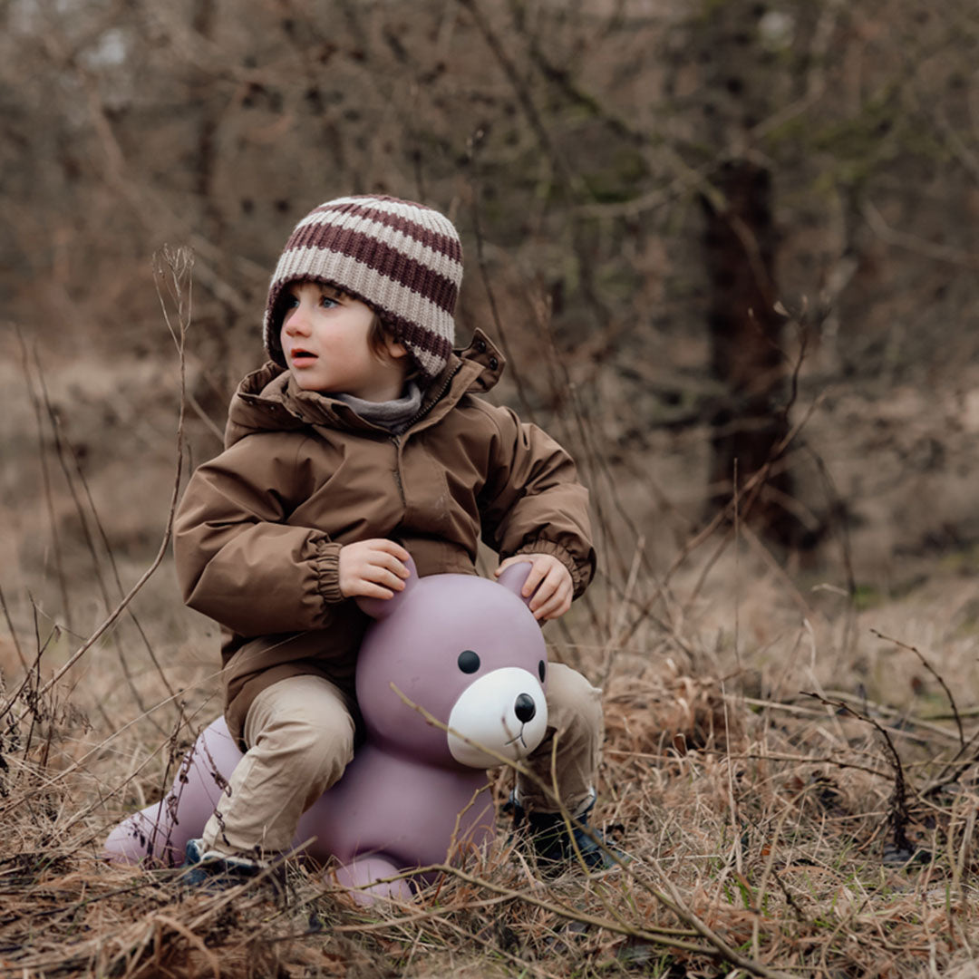 Een kind zit op het find that hippo paarse skippydier beer in een droog, winters landschap.