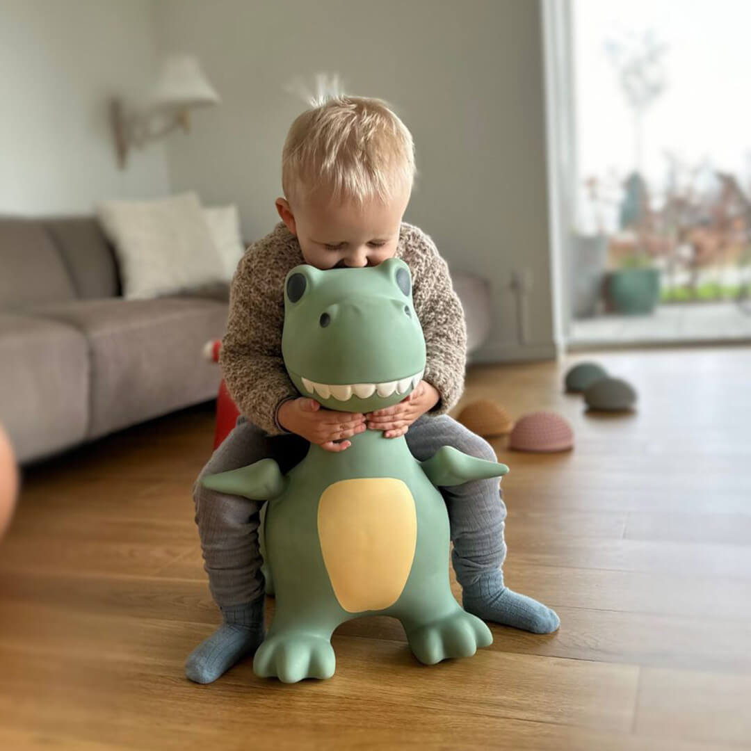 Een kind zit op de find that hippo skippydier dino en knuffelt de kop van het groene opblaasbare speelgoeddier.
