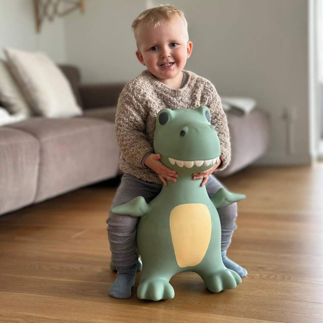 Een lachend kind zit op de find that hippo skippydier dino in een woonkamer.