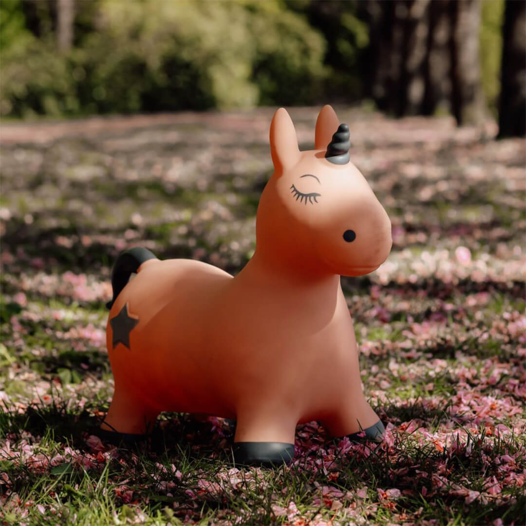 Het find that hippo roze eenhoorn skippydier staat in het gras tussen roze bloemblaadjes in een park.