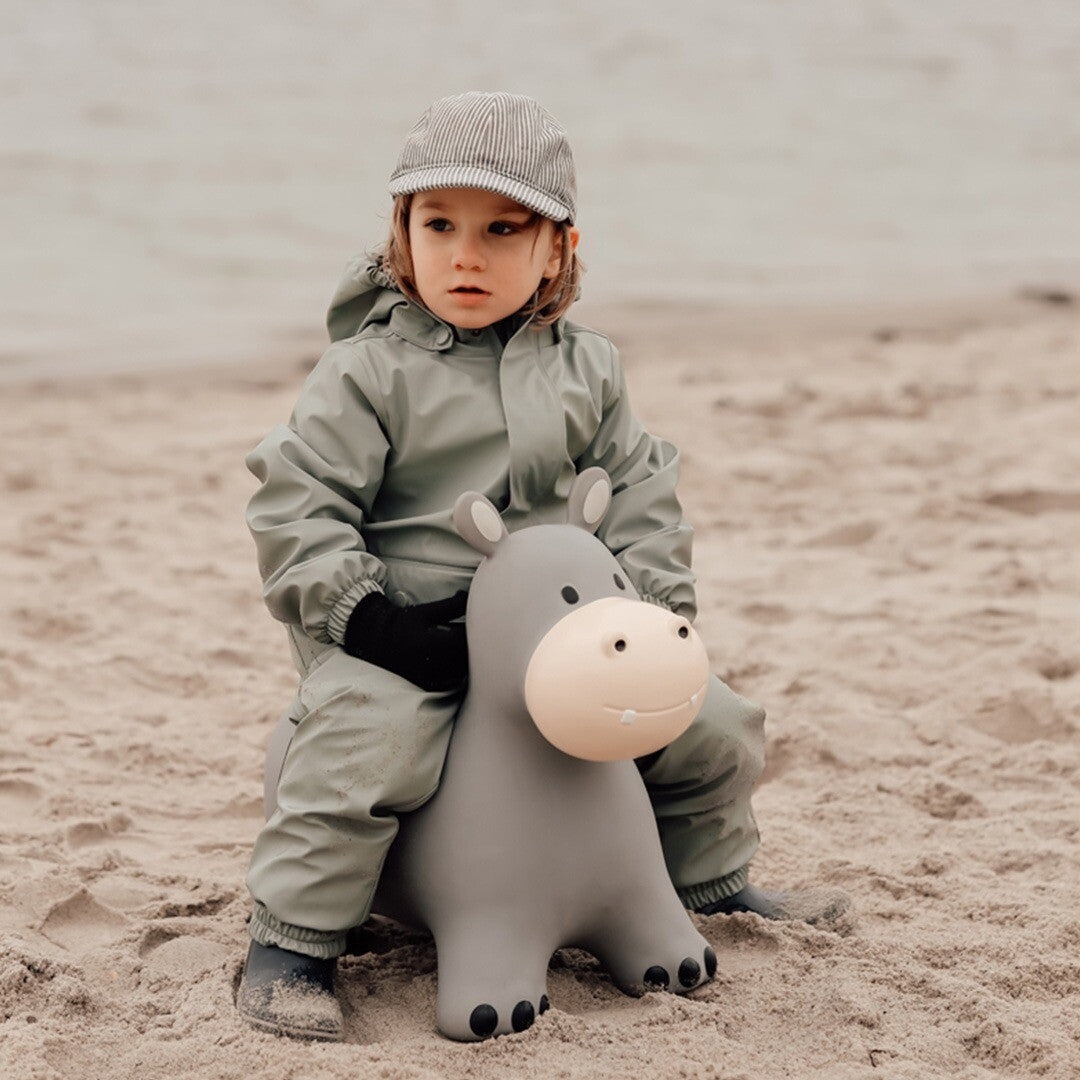 Een kind zit op het find that hippo grijze skippydier nijlpaard op een zandstrand.