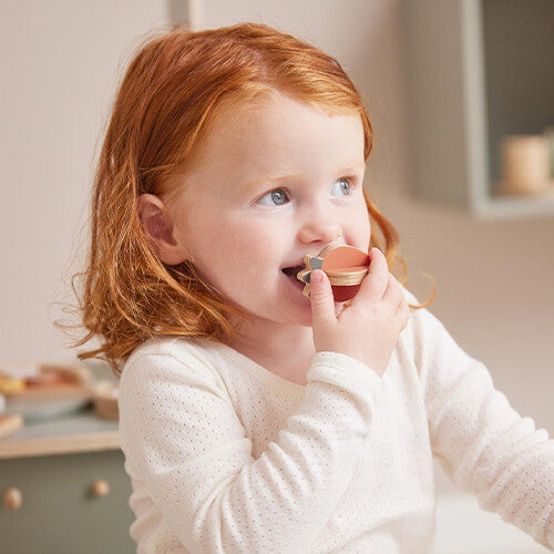 Een kind met rood haar speelt met een stukje Flexa houten speelgoedfruit.