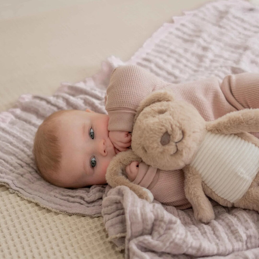 Een baby ligt op een deken en kijkt naar het bruine pluchen knuffelkonijn.