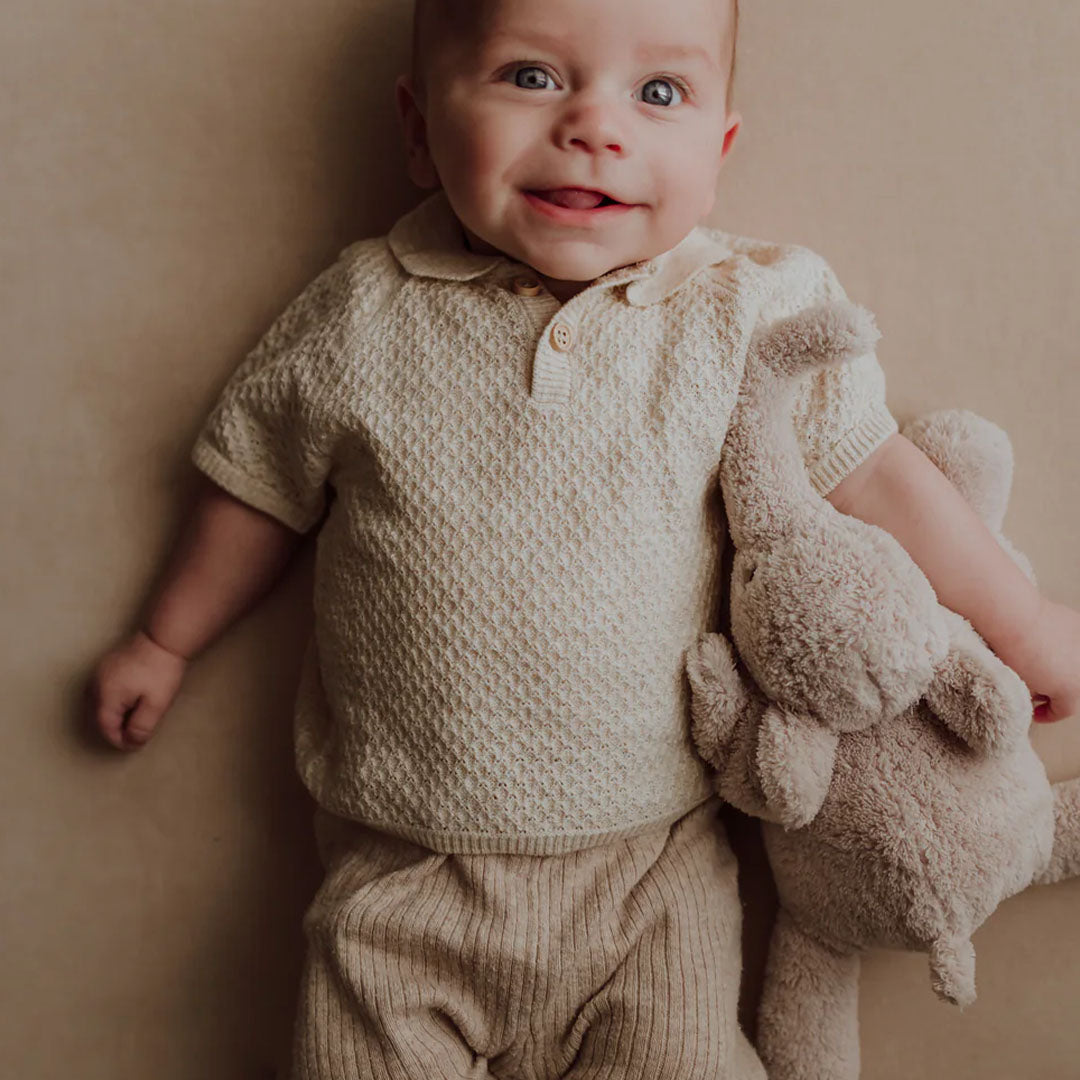 Een lachende baby ligt op de rug en knuffelt met de beige flow amsterdam pluchen olifant.