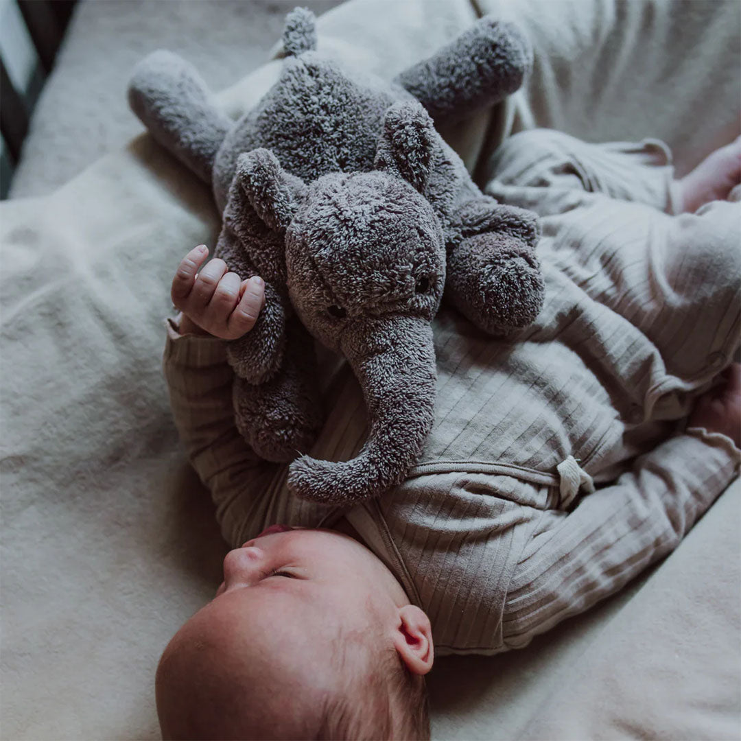 Een baby ligt op de rug en knuffelt met de grijze knuffelolifant.
