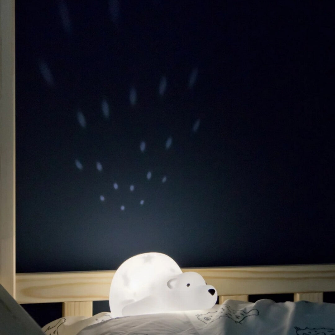 De Flow Amsterdam nachtlamp beer projecteert sterren op de muur naast een bed.
