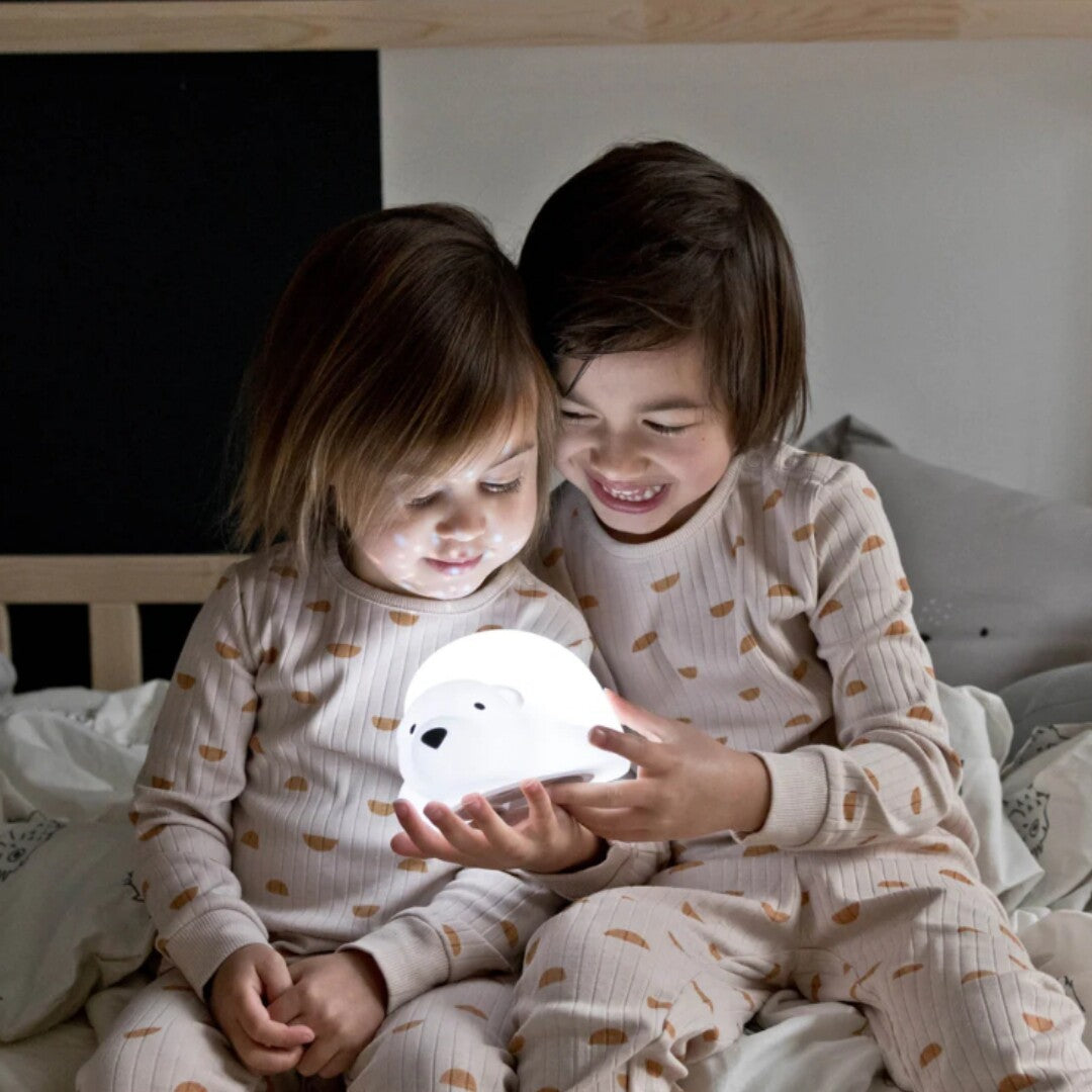 Twee kinderen in pyjama houden de oplichtende Flow Amsterdam nachtlamp beer vast op bed.