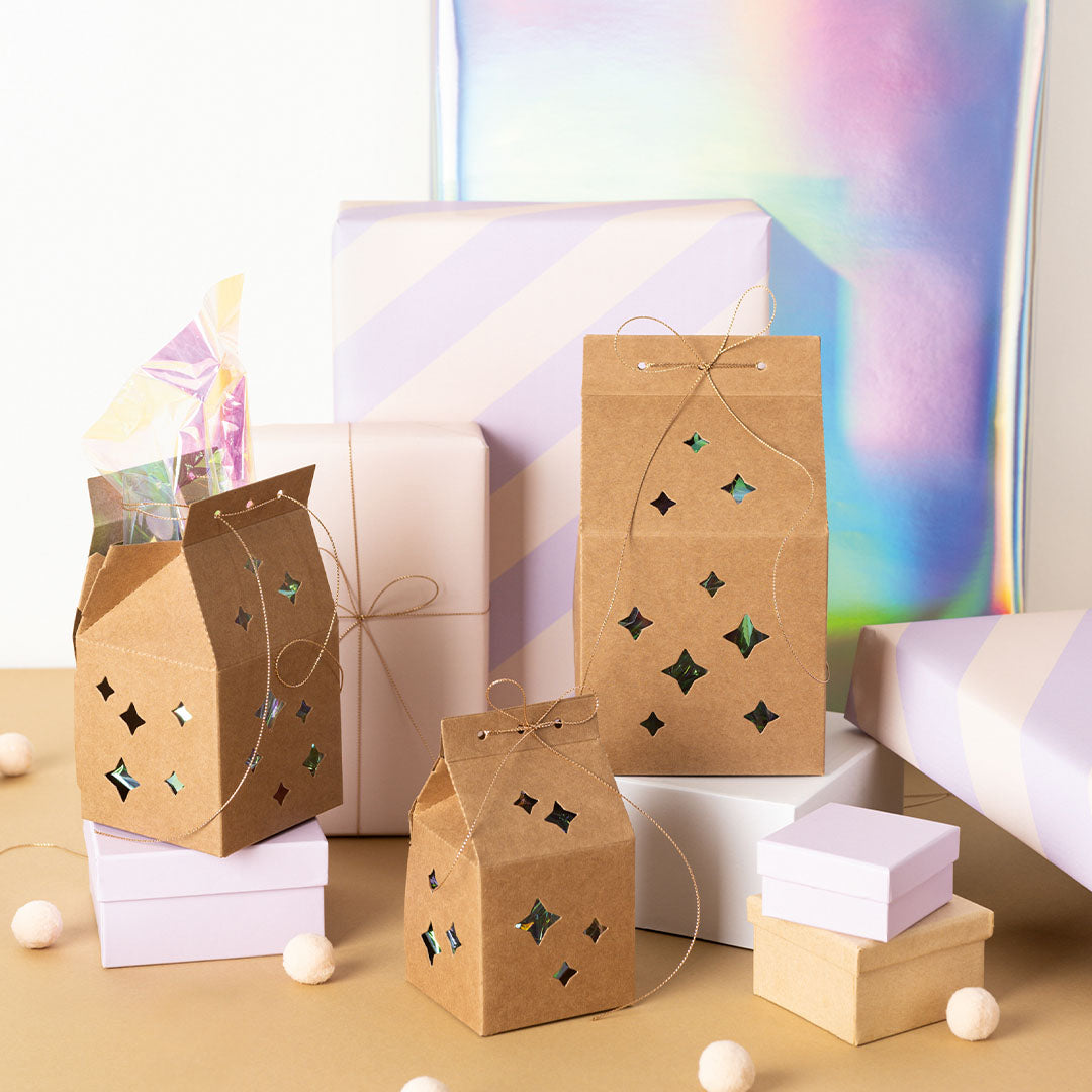 Drie Folia papieren cadeauzakjes met sterrenuitsparingen, staand op kleine cadeauboxen.