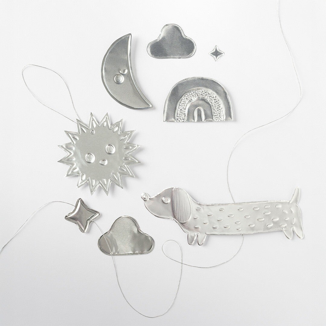 Zilveren, reliëf figuren van aluminium embossingfolie, waaronder een zon, maan, wolken, sterren, een regenboog en een hond, op een witte achtergrond.