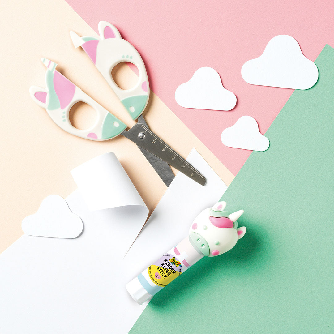 De Folia eenhoorn kinderschaar open naast een lijmstift en papieren wolkjes op een pastelkleurige ondergrond.