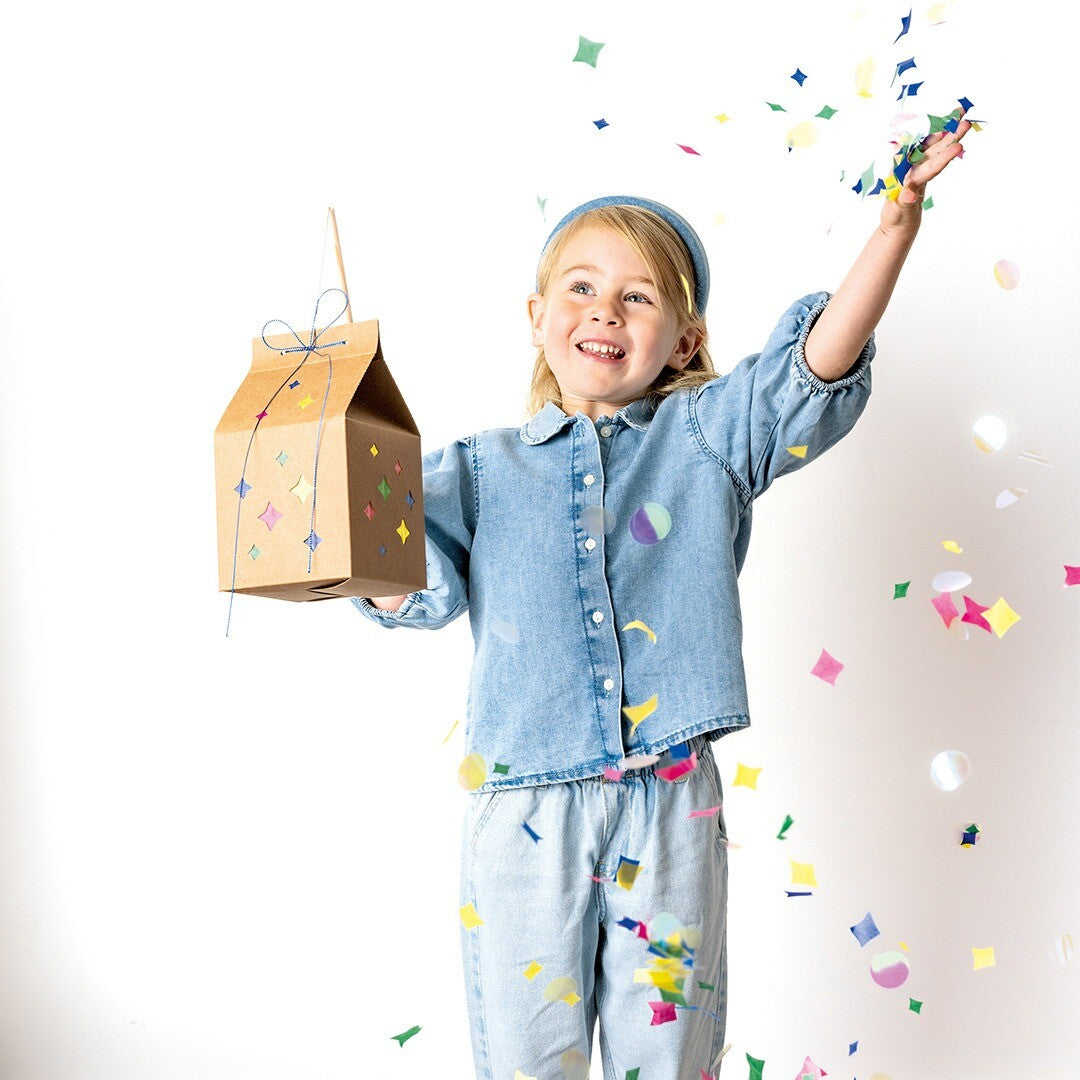 Blij kind met de folia knutselset lantaarn met sterren, omringd door vallende confetti.