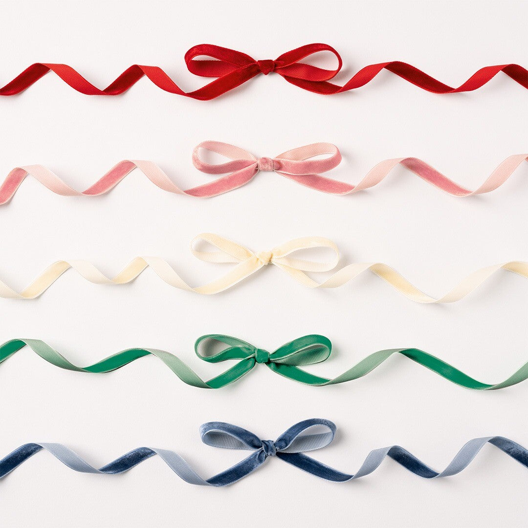 Vijf fluwelen linten in rood, roze, crème, groen en blauw, elk gestrikt als een strik op een witte achtergrond.