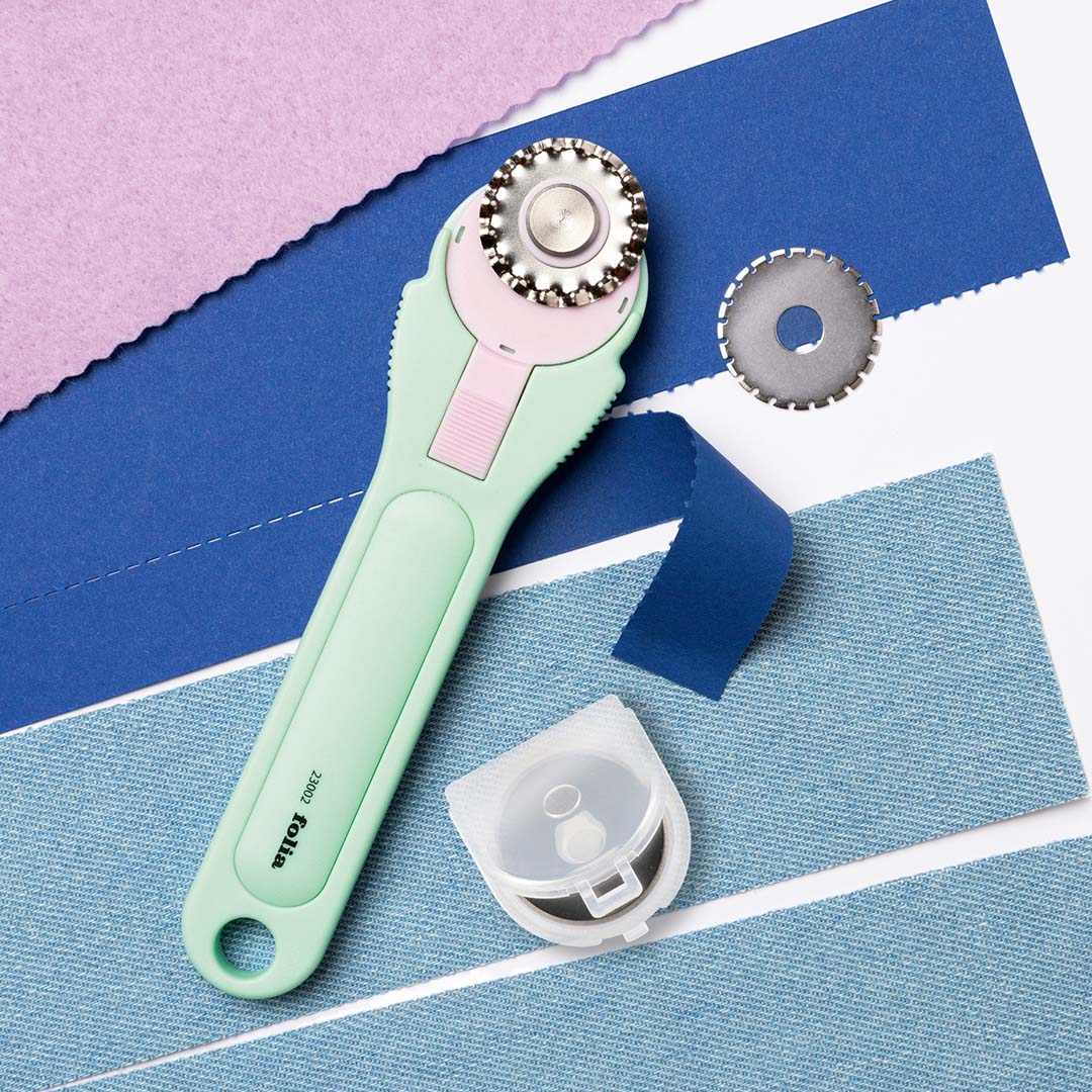 Folia snijroller met gekarteld mesje snijdt door blauwe stof, met extra mesjes en stoffen in verschillende kleuren.