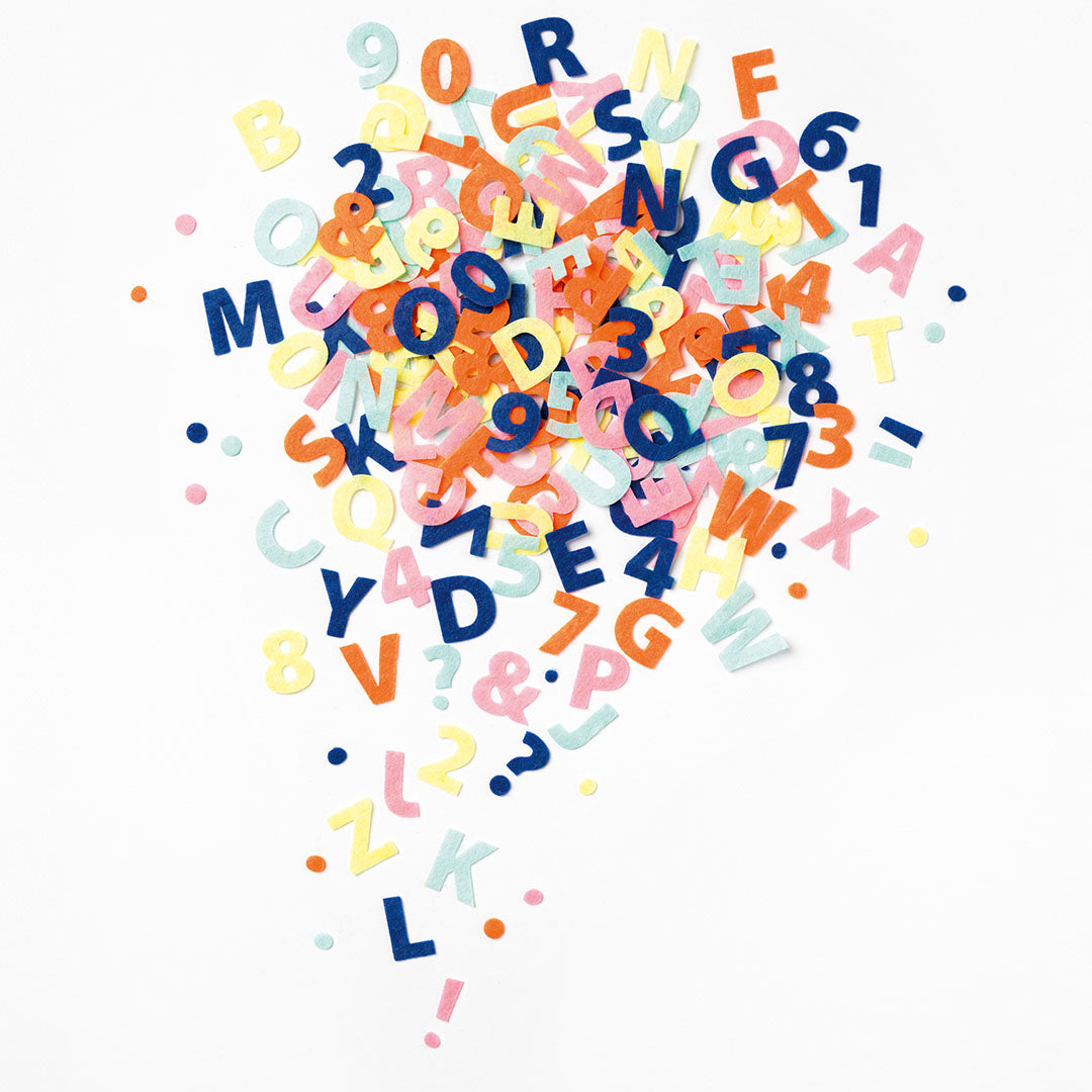 Een grote verzameling veelkleurige vilten letters en cijfers verspreid over een witte ondergrond.