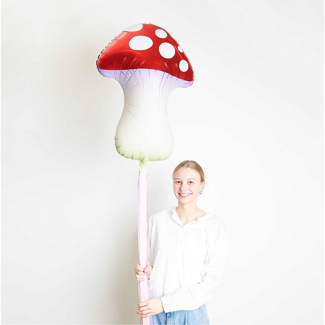 Een lachende vrouw houdt de grote Rico Design folieballon in de vorm van een paddenstoel vast.