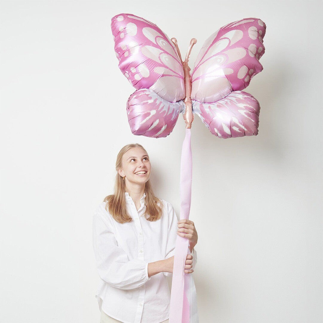 Een vrouw houdt een grote roze vlinder folieballon vast.