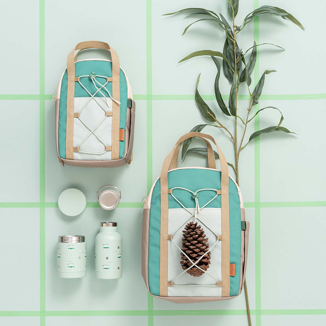 Twee Fresk peuterrugzakken in groen en beige, met een waterfles en voedselpot op een groene ondergrond.