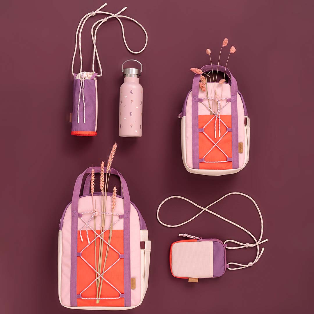 Een collectie Fresk schoolrugzakken en bijpassende accessoires in roze, paars en oranje op een paarse ondergrond.