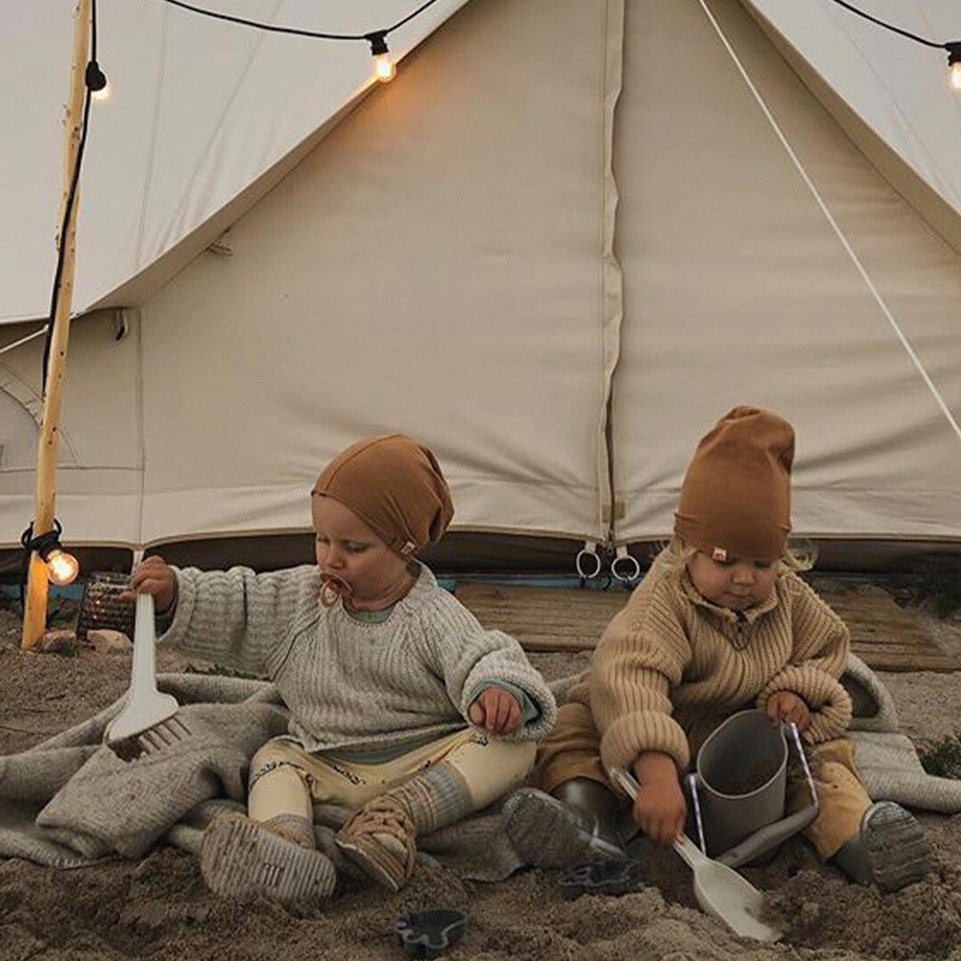 Twee baby's spelen in het zand met een grijze Scrunch emmer en schepjes voor een tent.