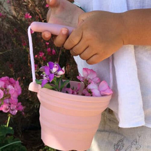 Een kind draagt een roze funkit Scrunch opvouwbare emmer gevuld met bloemen.