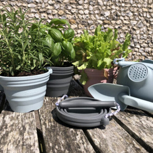 Een collectie Scrunch siliconen zandbakspeelgoed en plantenpotten in verschillende kleuren op een houten tafel.