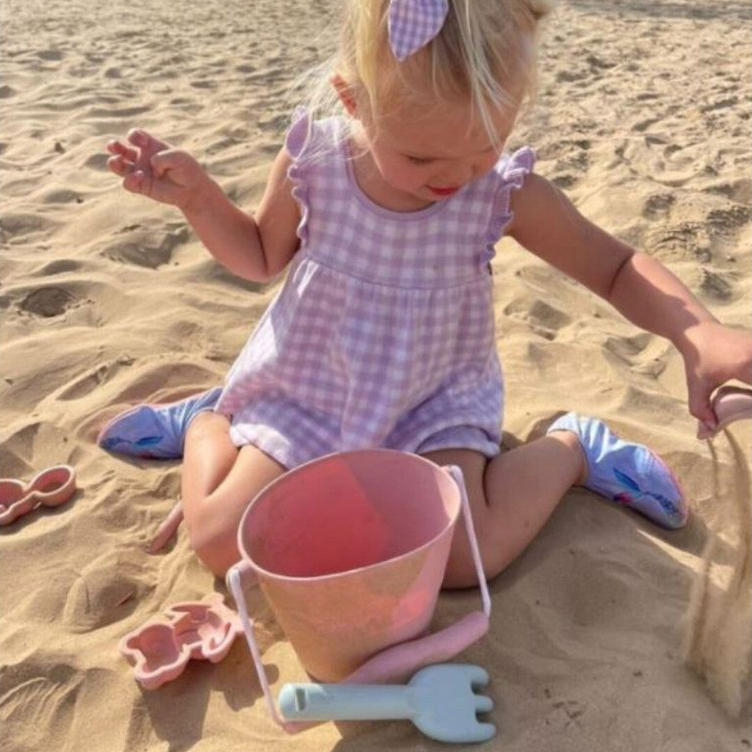 Een kind speelt in het zand met een emmer en een hark, demonstratie van zandspeelgoed.