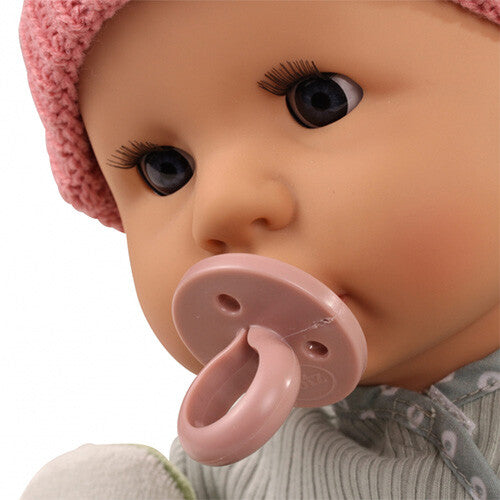 Close-up van het gezicht van de babypop met een roze speen in de mond en een roze muts.