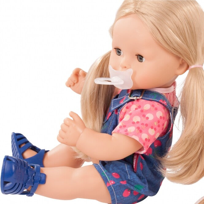 Detail van de Götz babypop Maxy Aquini Cherry Kiss met speen, blonde staartjes en denim tuinbroek met kersenpatroon.