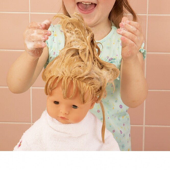 Een kind wast het haar van de Götz babypop Maxy Aquini Cherry Kiss, die in een witte handdoek is gewikkeld.
