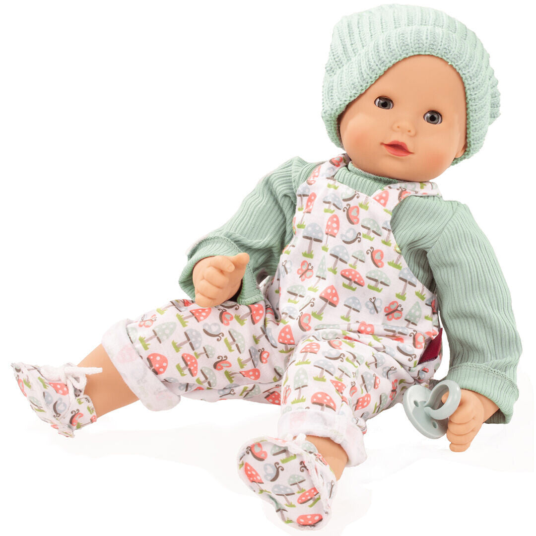 Gotz babypop Maxy Muffin met groene muts en tuinbroek met paddenstoelenprint, zittend en een speen vasthoudend.