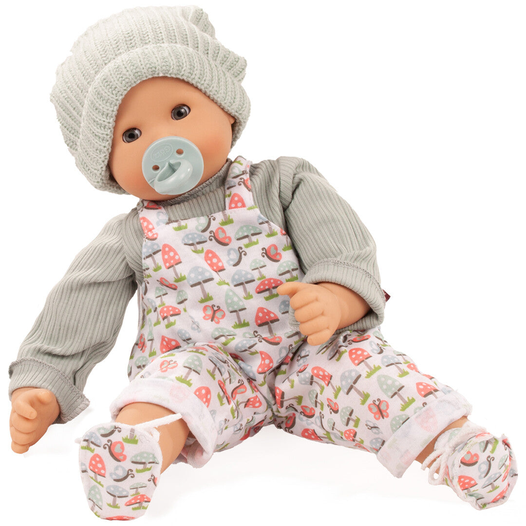 Gotz babypop Maxy Muffin met groene muts en tuinbroek met paddenstoelenprint, zittend met een speen in de mond.