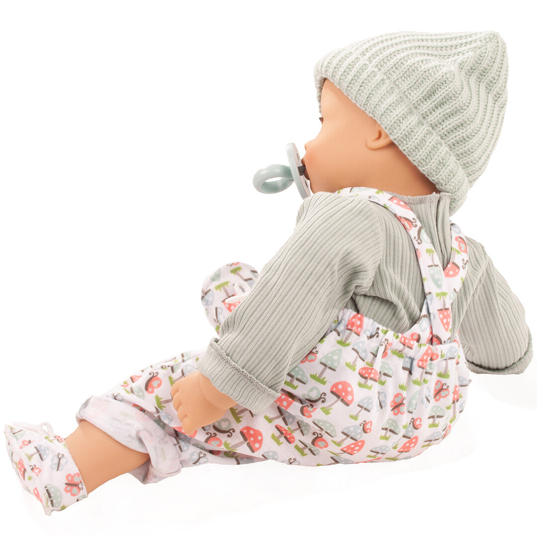 Gotz babypop Maxy Muffin, zijaanzicht, met groene muts en tuinbroek met paddenstoelenprint en een speen in de mond.