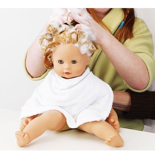 Een persoon wast het haar van de Gotz babypop Maxy Muffin, die een witte handdoek draagt.
