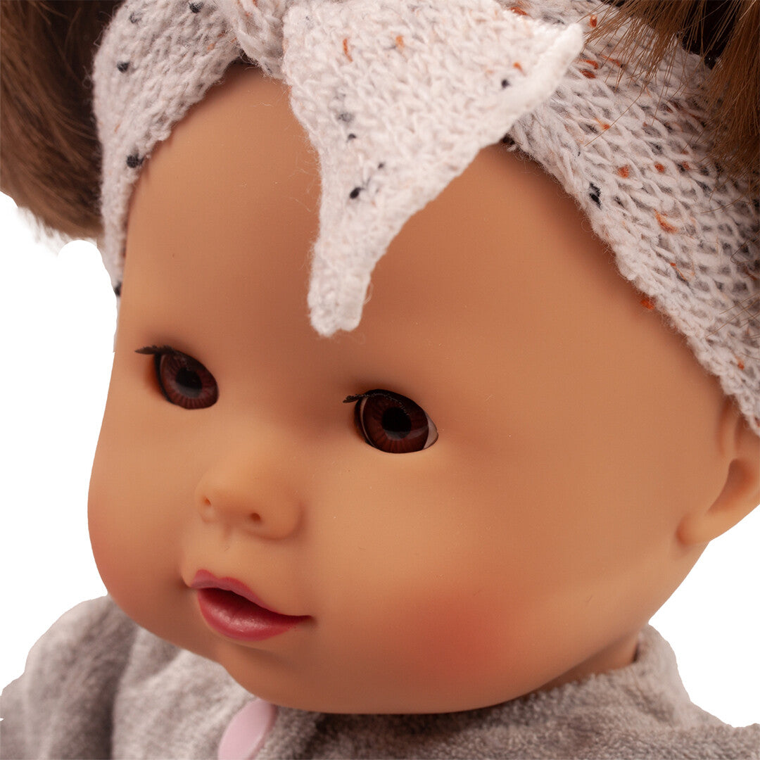 Close-up van het gezicht van de Gotz babypop met bruine ogen en een gebreide hoofdband.