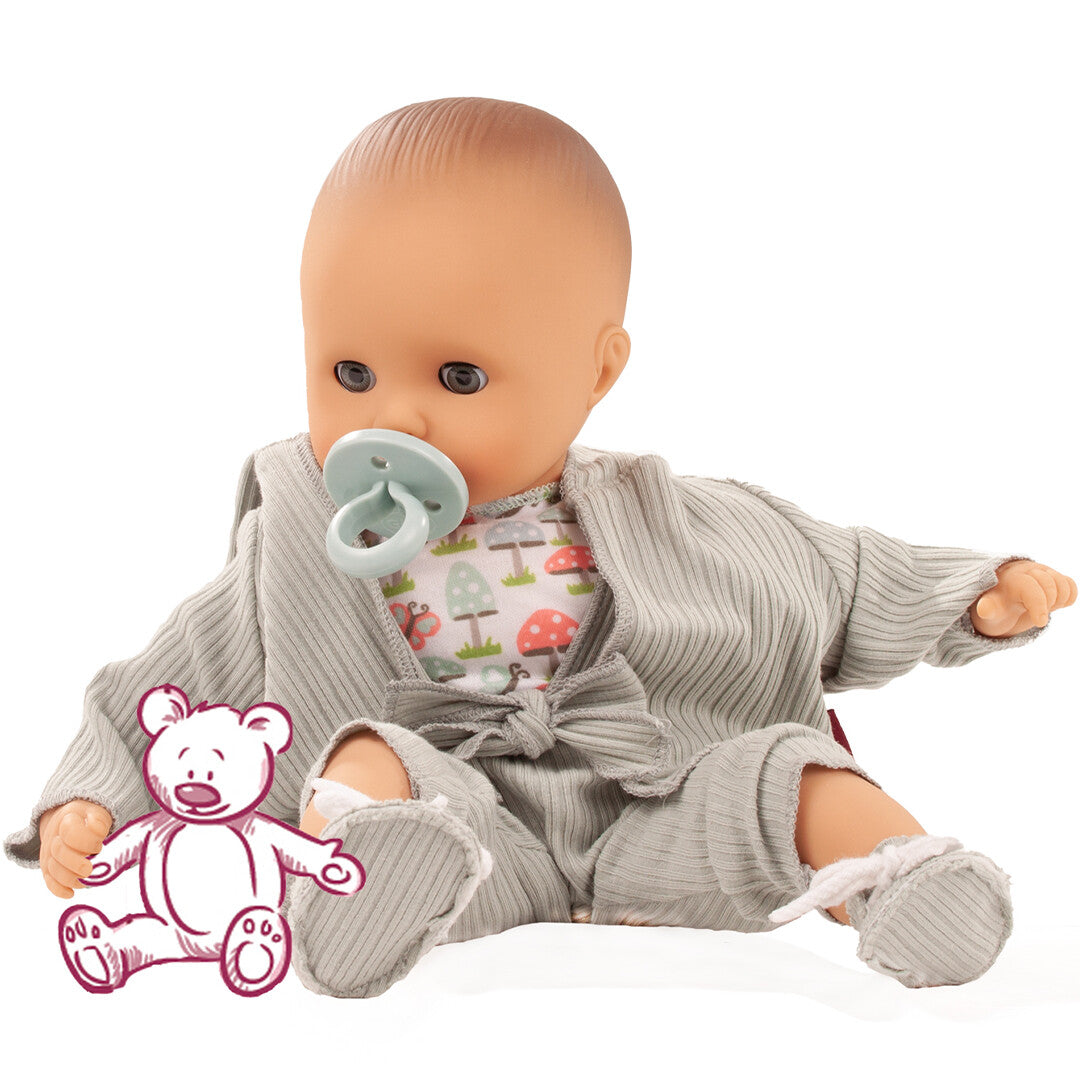 Götz babypop Muffin Glückspilz met speen, zittend in een grijze geribbelde outfit en een shirt met paddenstoelenpatroon, met een getekende teddybeer ernaast.