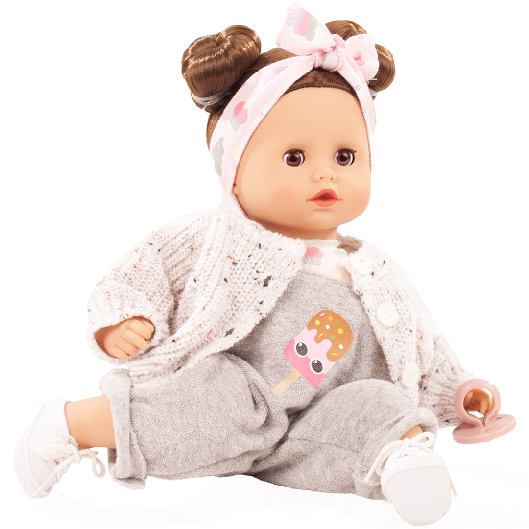 Götz babypop Muffin Popsicle zittend in een grijs pakje met roze vestje en hoofdband met cupcakes.